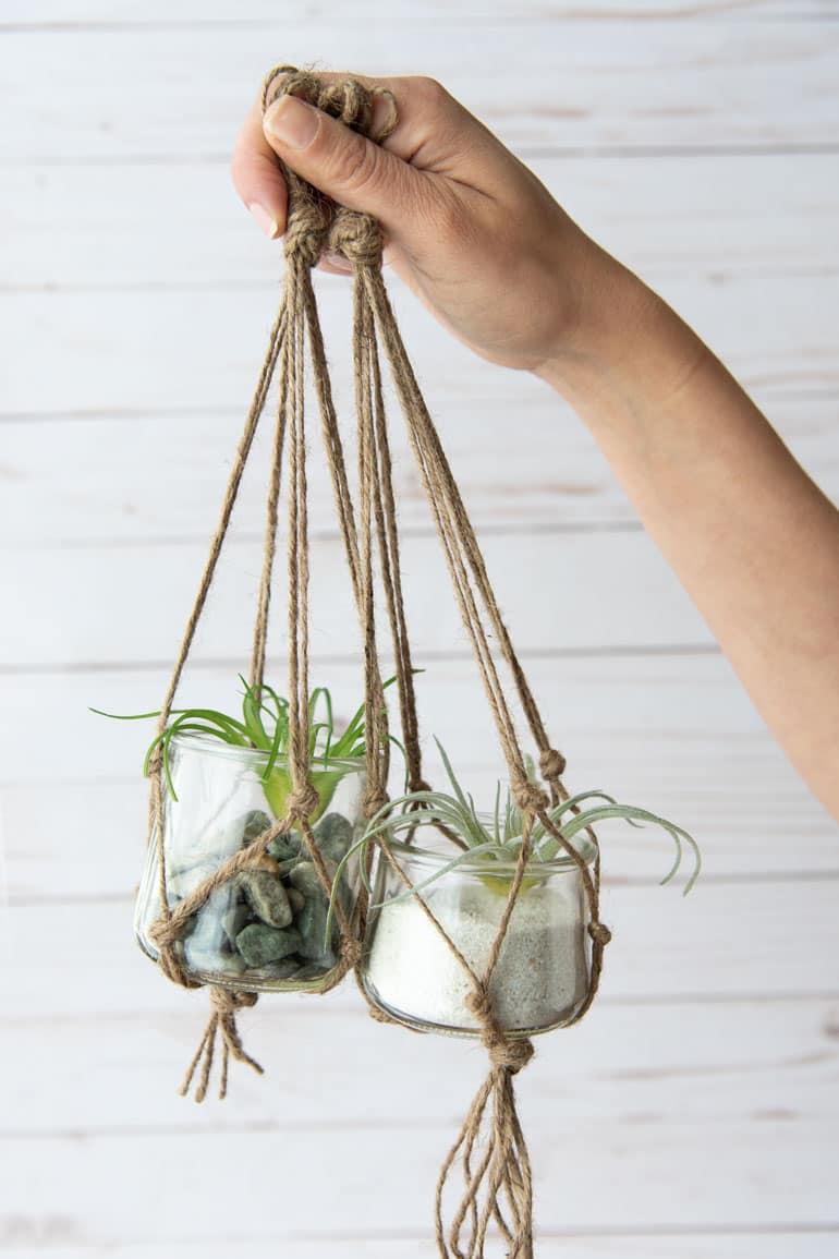 A hand holding two small macrame planters made from Oui by Yoplait yogurt glass jars.