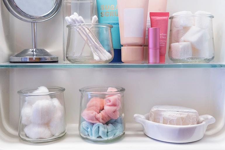 A variety of Oui by Yoplait yogurt jars reused as holders for different items in a bathroom.