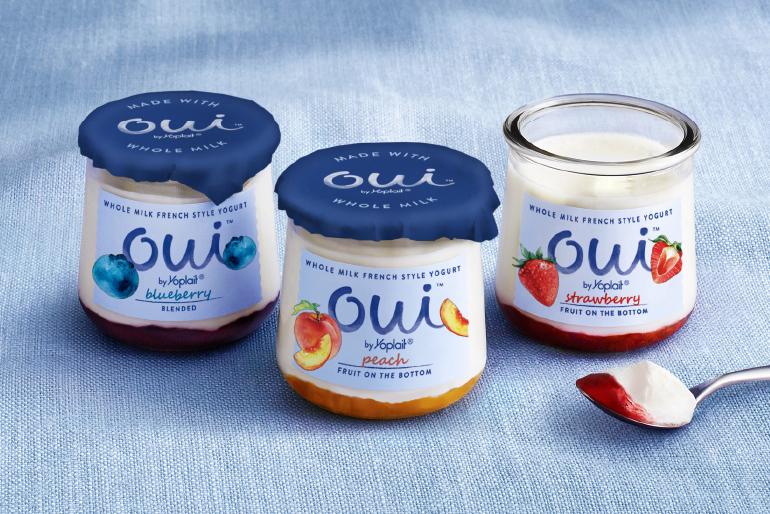 Jars of blueberry, peach and strawberry Oui by Yoplait yogurt on a blue tablecloth.